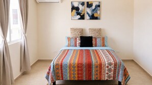 Ein Schlafzimmer mit einem Bett, einem Deckenventilator, einer Klimaanlage und zwei abstrakten Bildern an der Wand.