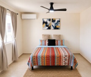Ein Schlafzimmer mit einem Bett, einem Deckenventilator, einer Klimaanlage und zwei abstrakten Bildern an der Wand.