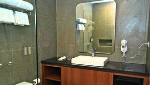 A modern bathroom with a large mirror, a white sink, and wooden cabinets.