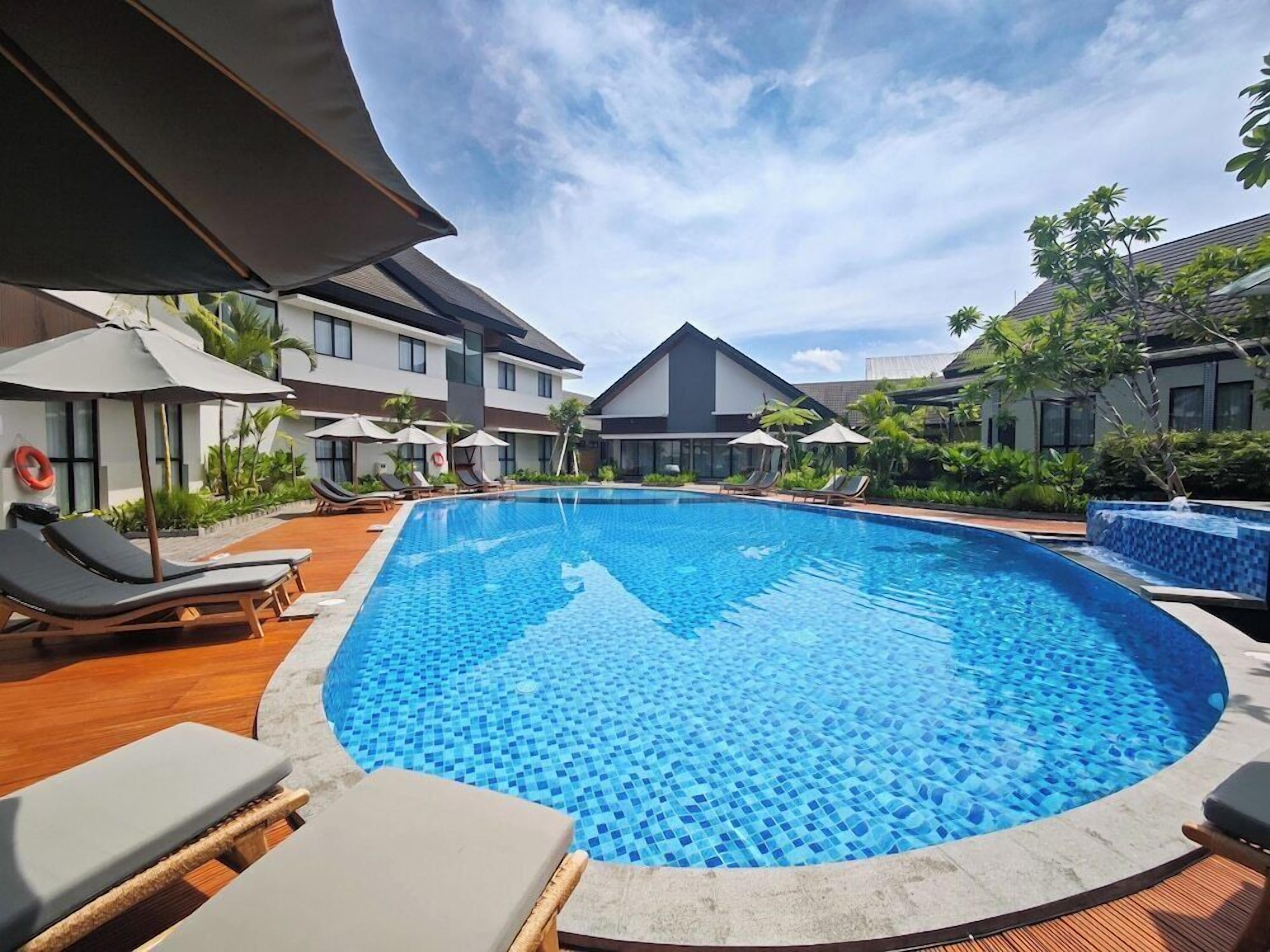 Ein Pool mit Liegestühlen und Sonnenschirmen, umgeben von Gebäuden im modernen Stil.