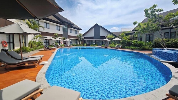 A swimming pool with lounge chairs and umbrellas, surrounded by buildings with a modern design.
