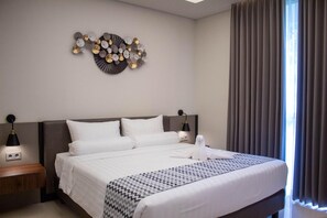 A hotel room with a large bed, two bedside tables, a wall-mounted light fixture, and a window with curtains.