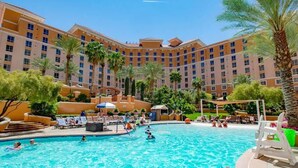 A hotel with a swimming pool surrounded by palm trees and lounge chairs.