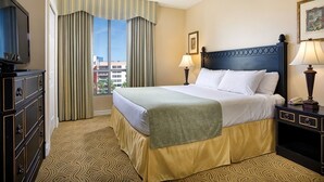 A hotel room with a bed, a television, a dresser, and a window with curtains.