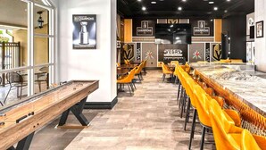 A sports bar with a long counter, tables, and chairs, featuring sports memorabilia and a large screen.