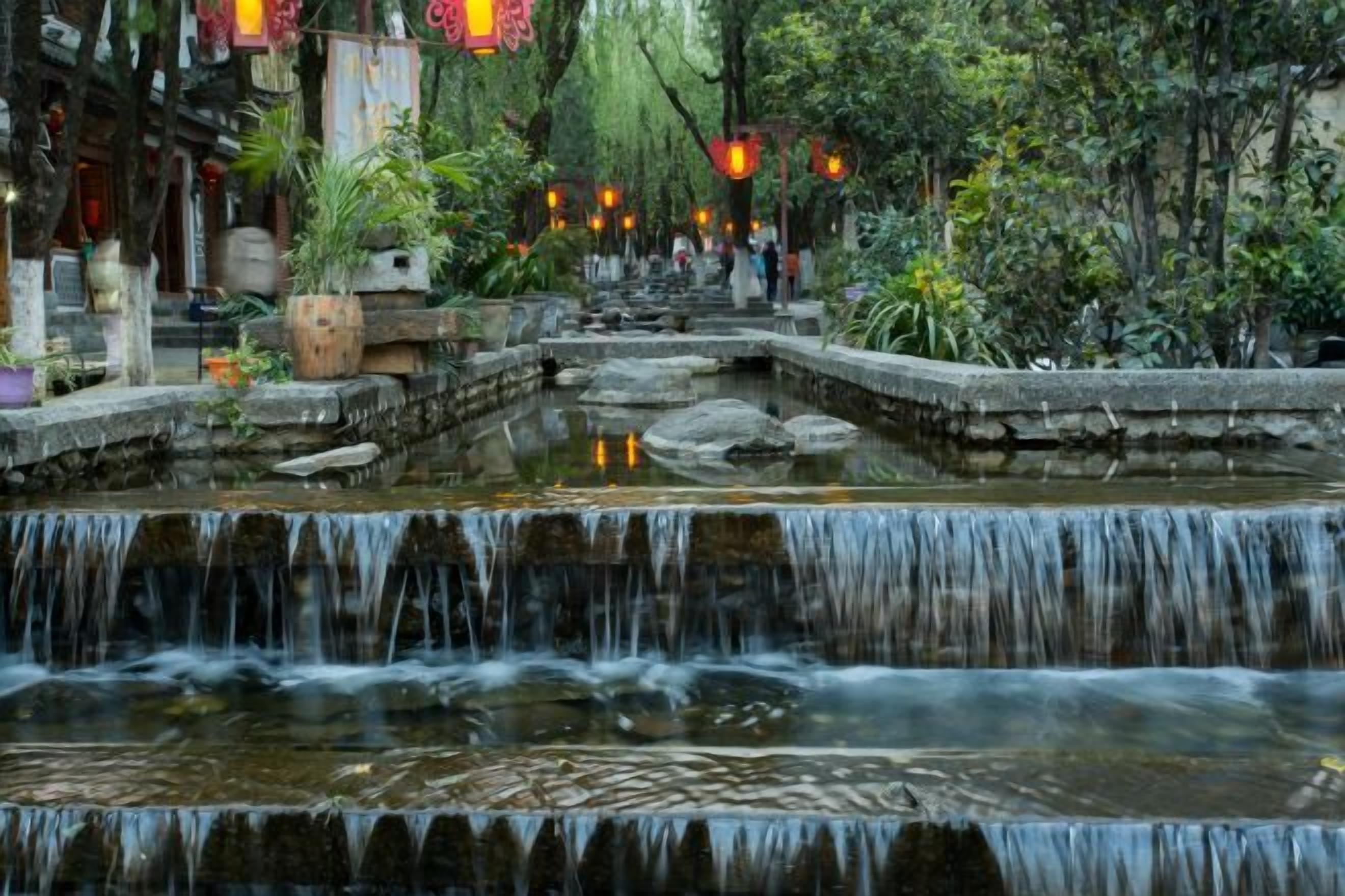 A traditional courtyard with a small waterfall, stone steps, and potted plants.