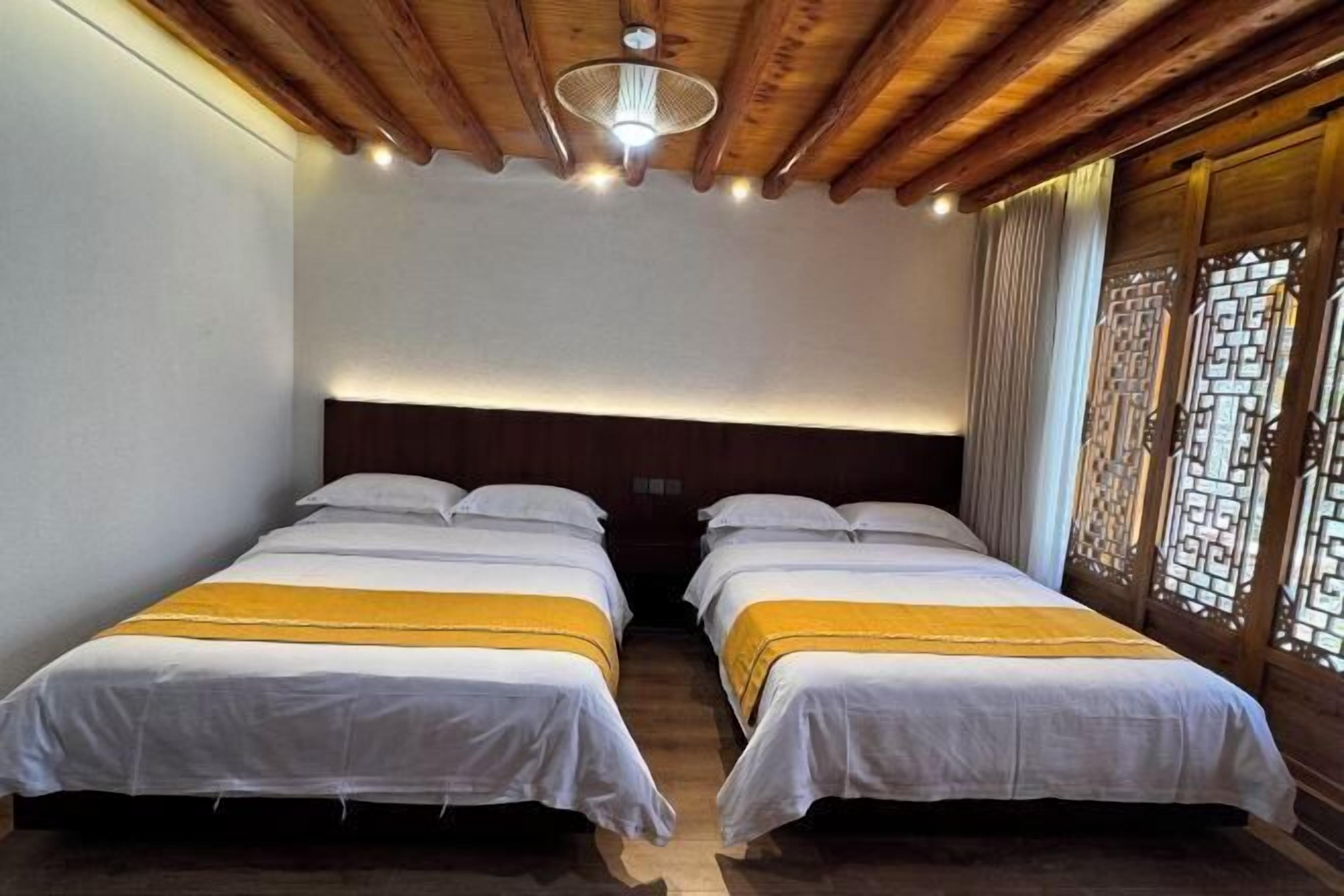 Habitación con dos camas, vigas de madera en el techo y una ventana tradicional con celosía decorativa.