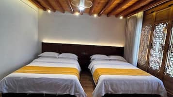 A room with two beds, wooden ceiling beams, and a traditional window with decorative lattice.
