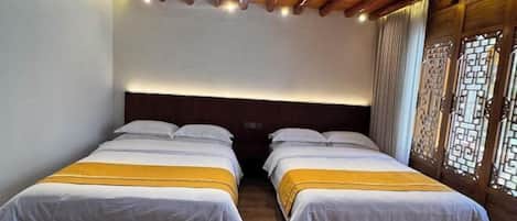 A room with two beds, wooden ceiling beams, and a traditional window with decorative lattice.