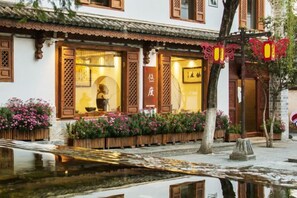 A traditional building with wooden doors and windows, a small garden with flowers, and a pond in front. - Youdu Inn (Dali City)