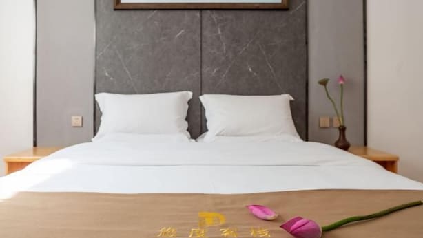 A hotel room with a large bed, a headboard with a marble finish, a painting above the bed, and a vase with flowers on the nightstand. - Youdu Inn (Dali City)