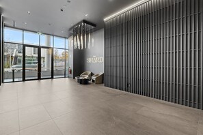 Ein moderner Empfangsbereich mit einer großen Glastür, einem an der Wand befestigten Schild mit der Aufschrift 'THE HARD' und einer Sitzecke mit zwei Sesseln.