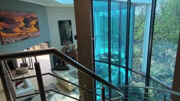 A modern interior with a glass staircase leading to a balcony with a view of trees.