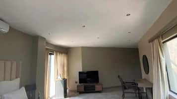 A room with a flat-screen TV on a stand, a dining table with chairs, and a window with curtains.