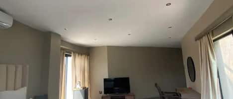 A room with a flat-screen TV on a stand, a dining table with chairs, and a window with curtains.