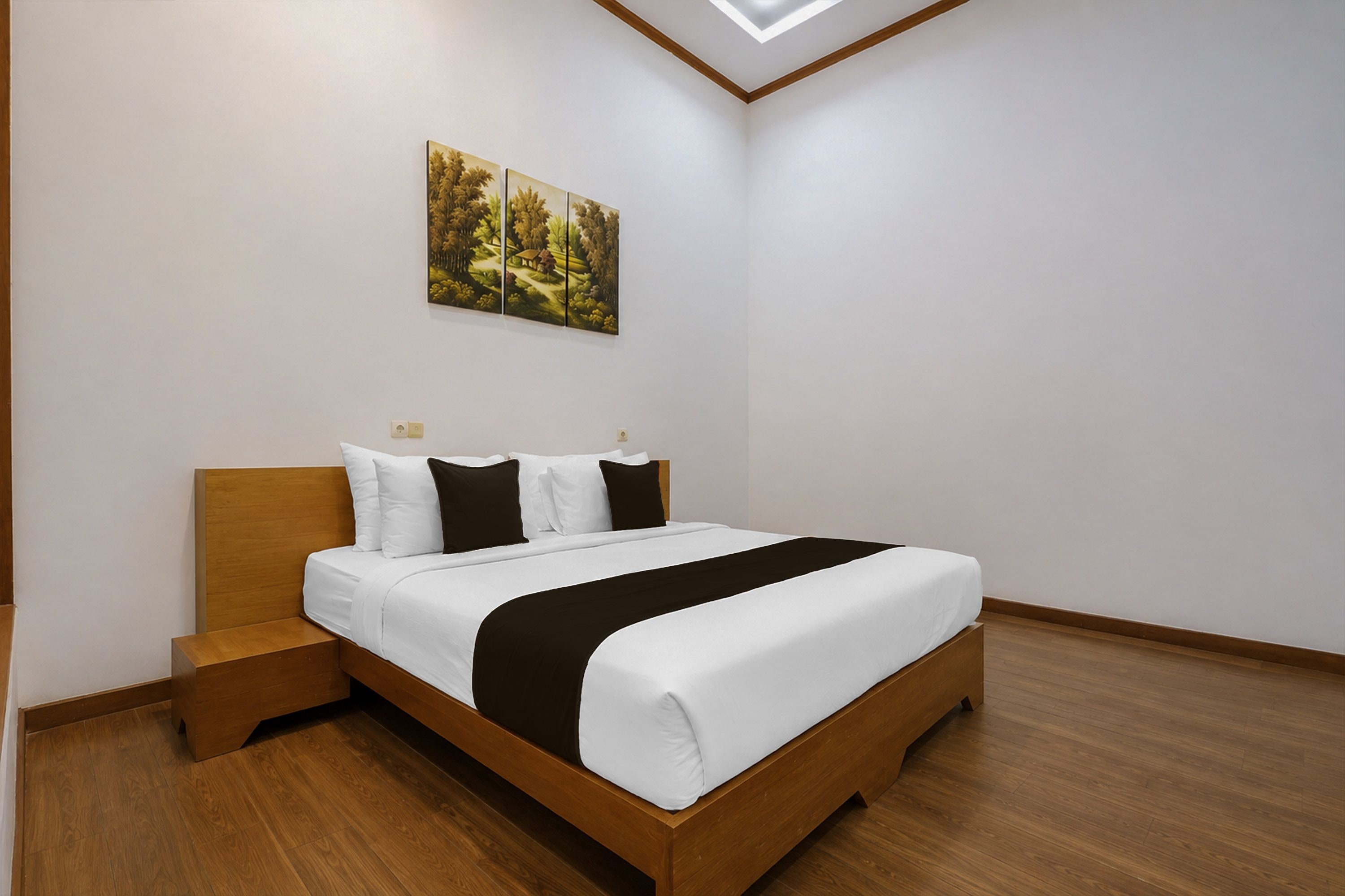 A bedroom with a wooden bed, white bedding, a nightstand, and a painting on the wall.