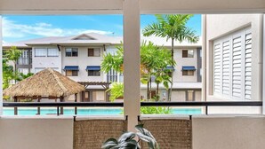 Uma varanda com vista para uma piscina, palmeiras e um edifício com telhado de palha.