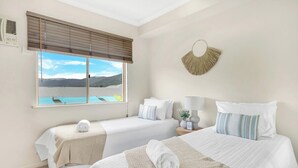 Quarto de hotel com duas camas, uma janela grande com vista, um ventilador fixado na parede e um objeto decorativo na parede.