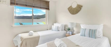 A hotel room with two beds, a large window with a view, a wall-mounted fan, and a decorative wall piece.