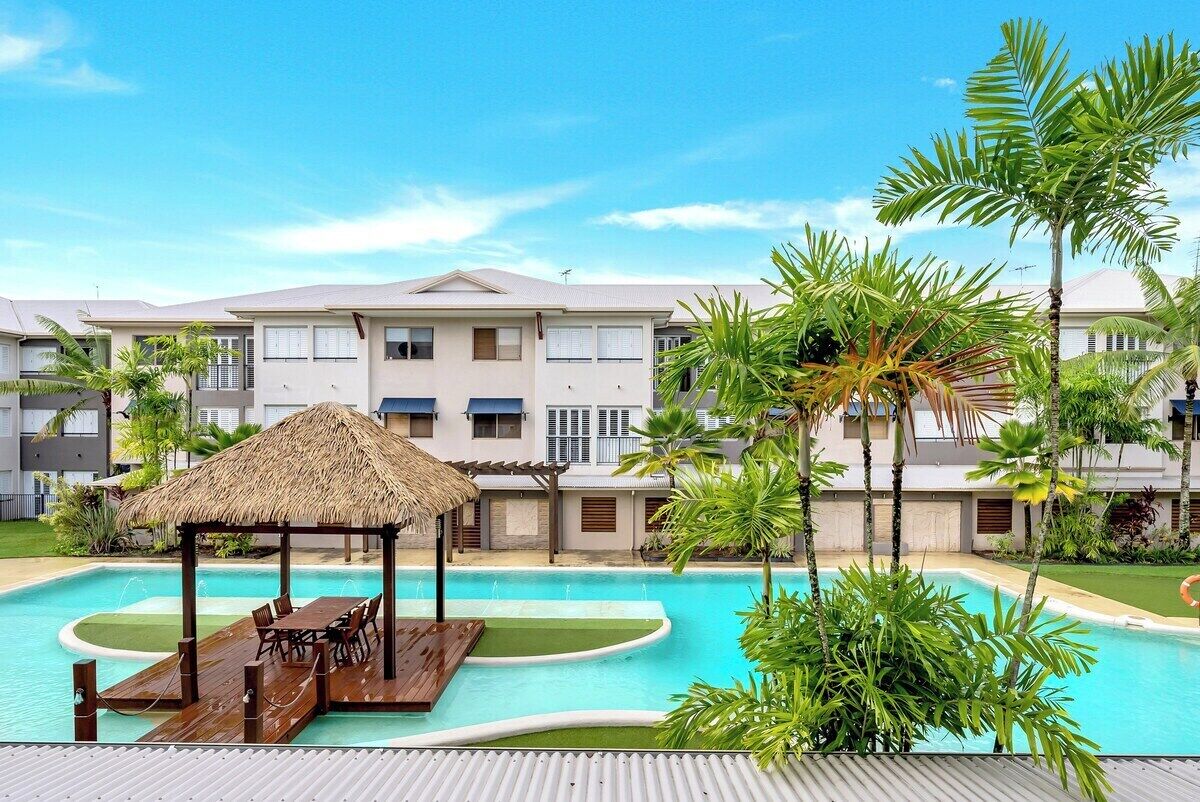 Um hotel com piscina, um gazebo com telhado de palha e plantas tropicais.
