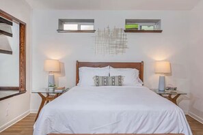 Une chambre avec un grand lit, deux tables de chevet avec des lampes, une fenêtre donnant sur un beau paysage et un élément décoratif mural.