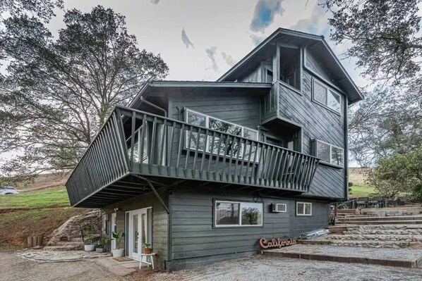 Une maison en bois à plusieurs niveaux, dotée d’un balcon, d’un garage et d’un petit porche à l’avant.