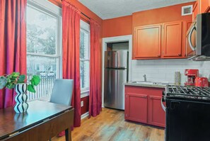 A kitchen with red cabinets, a stainless steel refrigerator, a stove, and a dining table with a chair. - 1BR The Montrose W Main 02, Downtown, Med Center (Houston)