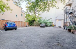 Una calle residencial con dos coches aparcados, una valla de madera y un edificio con escaleras de incendios.