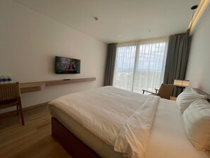 Quarto de hotel com uma cama grande, televisão na parede, escrivaninha com cadeira e janela com cortinas.