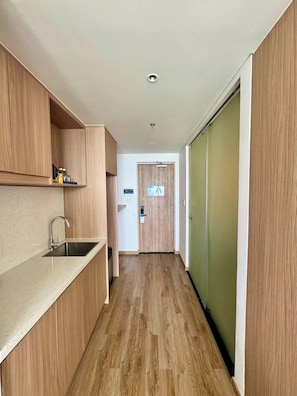 A narrow hallway with a kitchen area on the left, featuring a sink and wooden cabinets. - Walk to Beach| lovely AP with pool for honeymoon (Da Nang)