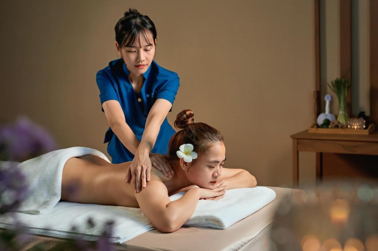 A person receiving a massage in a room with a wooden side table and a mirror.