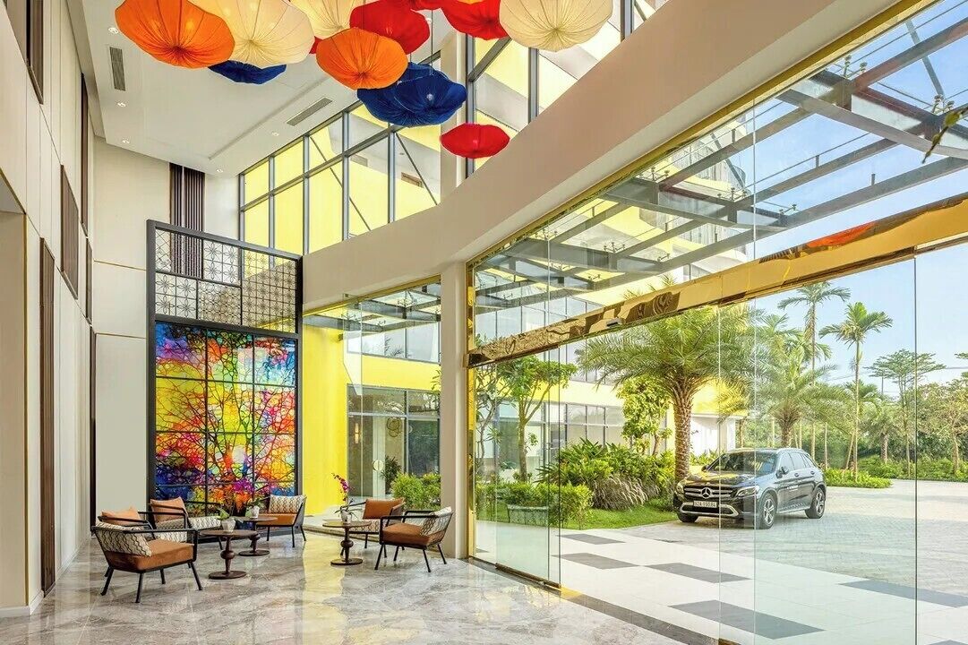 A hotel lobby with a glass entrance, a colorful abstract wall, and a seating area with chairs.