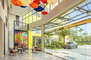 A hotel lobby with a glass entrance, a colorful abstract wall, and a seating area with chairs. - Walk to Beach| lovely AP with pool for honeymoon (Da Nang)
