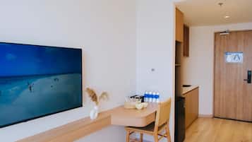 A room with a large flat-screen TV on the wall, a wooden table with a chair, a basket, and bottled water.