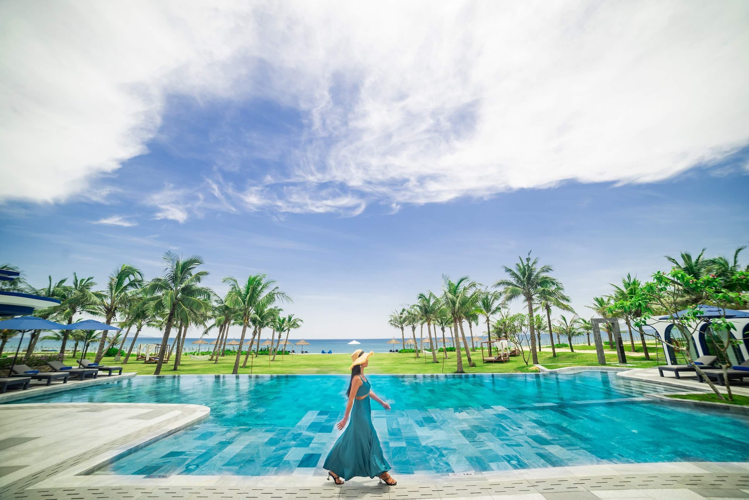 A pool area with a clear sky, palm trees, and a view of the sea.