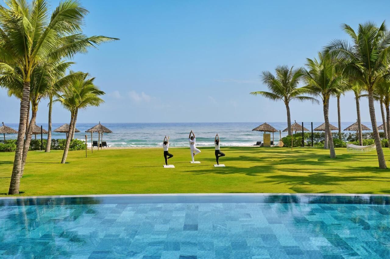 Un espace aménagé au bord de la piscine, offrant une vue sur l’océan, les palmiers et comprenant un tapis de yoga.