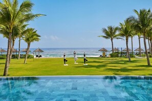 Área à beira da piscina com vista para o oceano, palmeiras e um tapete de yoga.