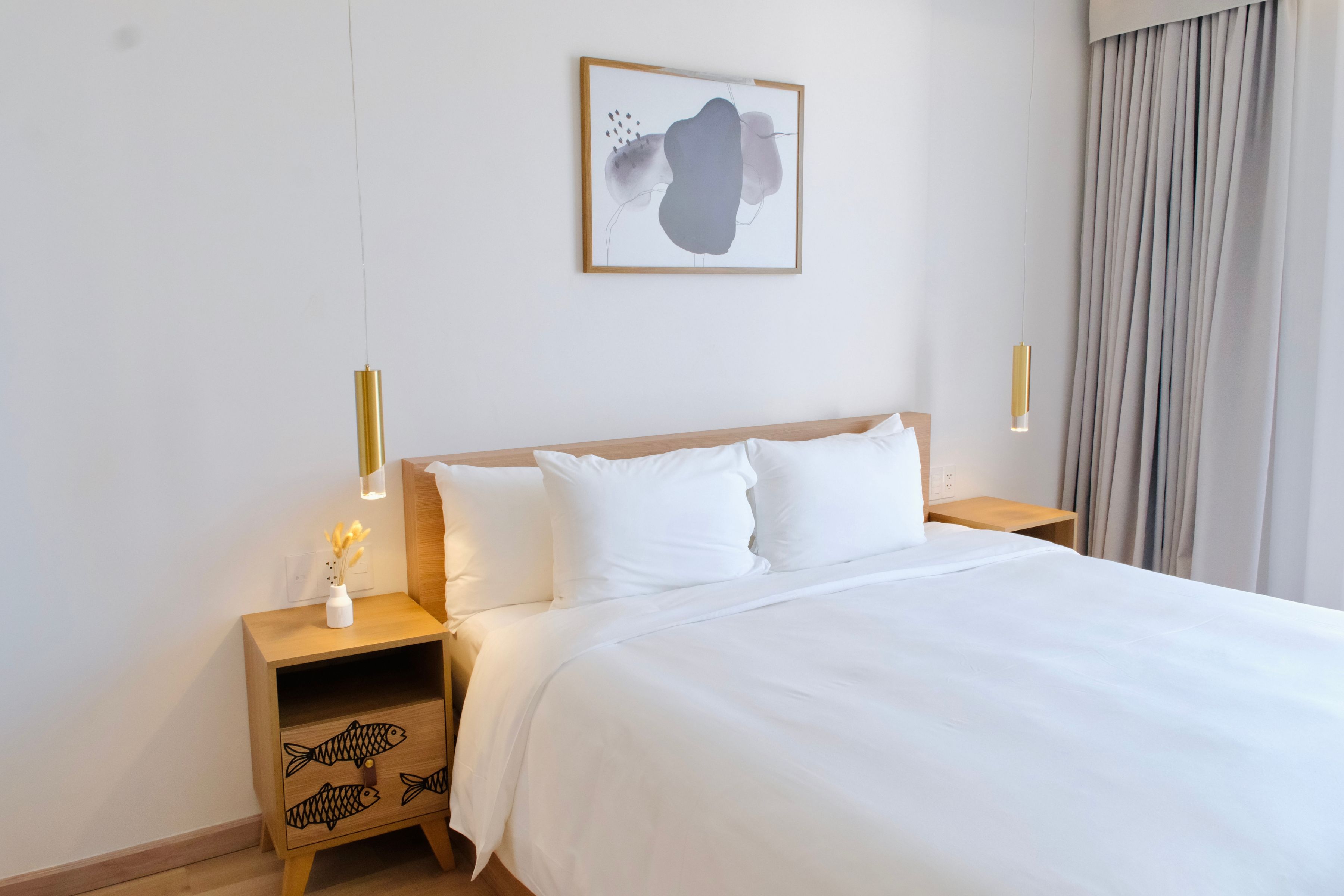 Quarto de hotel com uma cama grande, mesinhas de cabeceira de madeira, uma obra de arte na parede e vista para cortinas externas.