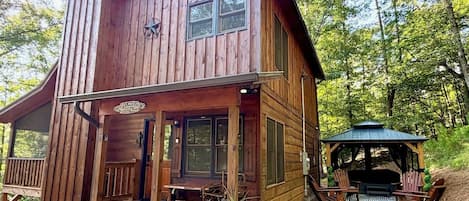 A wooden cabin with a porch, a covered outdoor seating area, and a gravel pathway.