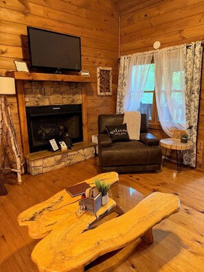 A cozy cabin interior with a stone fireplace, leather sofa, and a unique wooden coffee table. - Charming Cabin in the clouds with hot tub, screen porch and fireplace (Ellijay)