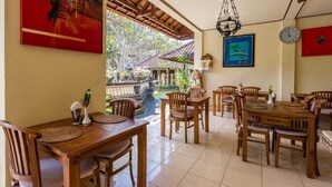 A dining area with wooden tables and chairs, a ceiling fan, and a view of a traditional building outside.