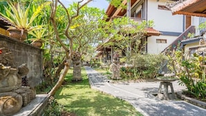 A courtyard with a pathway, stone statues, and lush greenery.