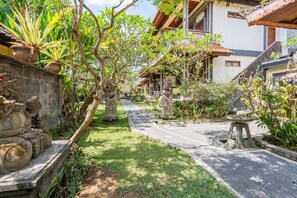 A courtyard with a pathway, stone statues, and lush greenery.