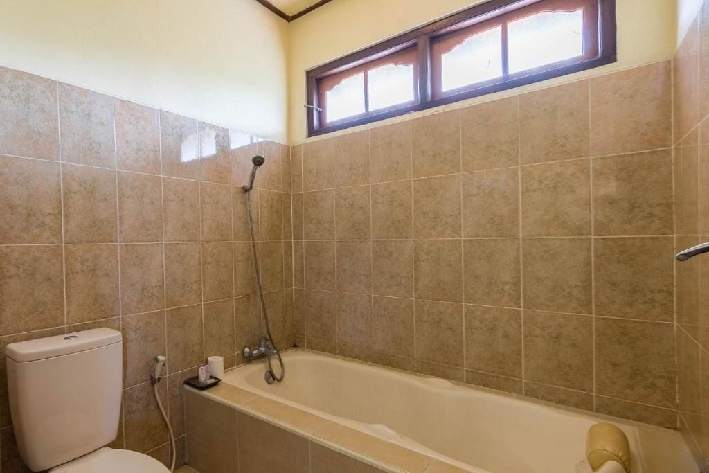 A bathroom with a bathtub, toilet, and a window above the tub.