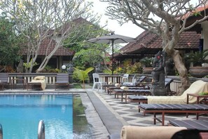 A poolside area with lounge chairs, a statue, and a tiled roof structure. - Sagitarius Inn Ubud (Ubud)