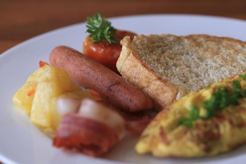 Um prato com linguiça, torradas, ovos mexidos e tomate.