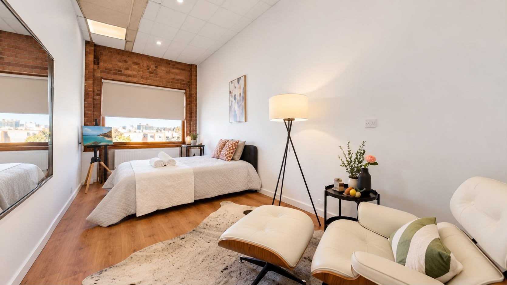 Bright modern bedroom with exposed brick, city views, and cozy lounge chair