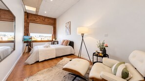 A modern bedroom with a bed, a desk, a chair, and a large window.