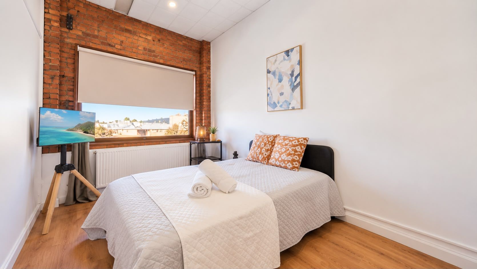 Bright double bedroom with exposed brick, large window, and cozy modern style