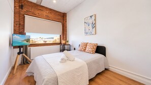A bedroom with a bed, a window with a view, a painting on the wall, and a lamp on a bedside table.
